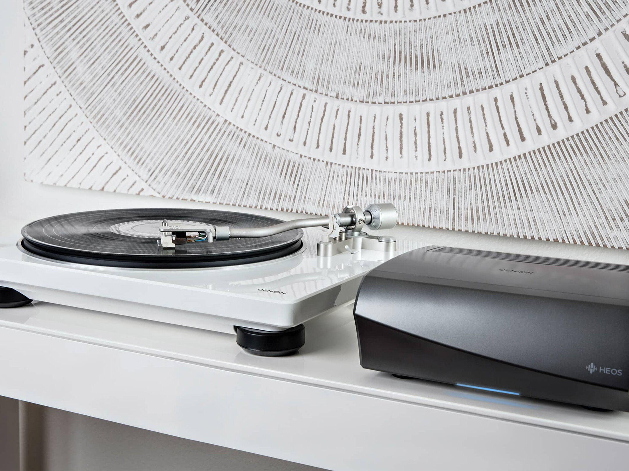 Pick-up Denon DP-400 alb, vedere laterală, cu platan vinil și braț metalic vizibil. Alături este amplificatorul Denon HEOS.
