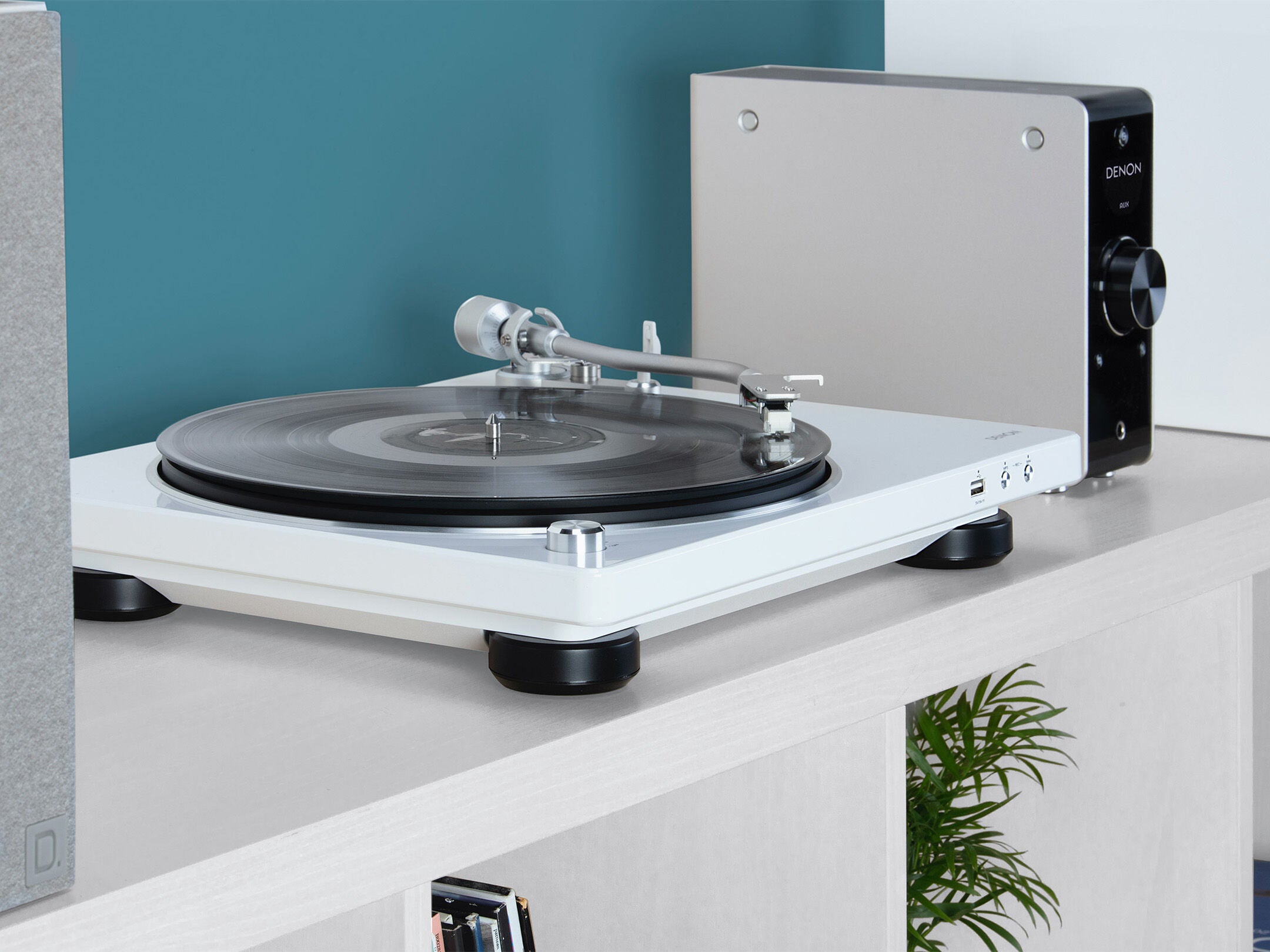 Pick-up Denon DP-450USB alb, vedere laterală, evidențiază brațul și porturile USB, pe un raft.
