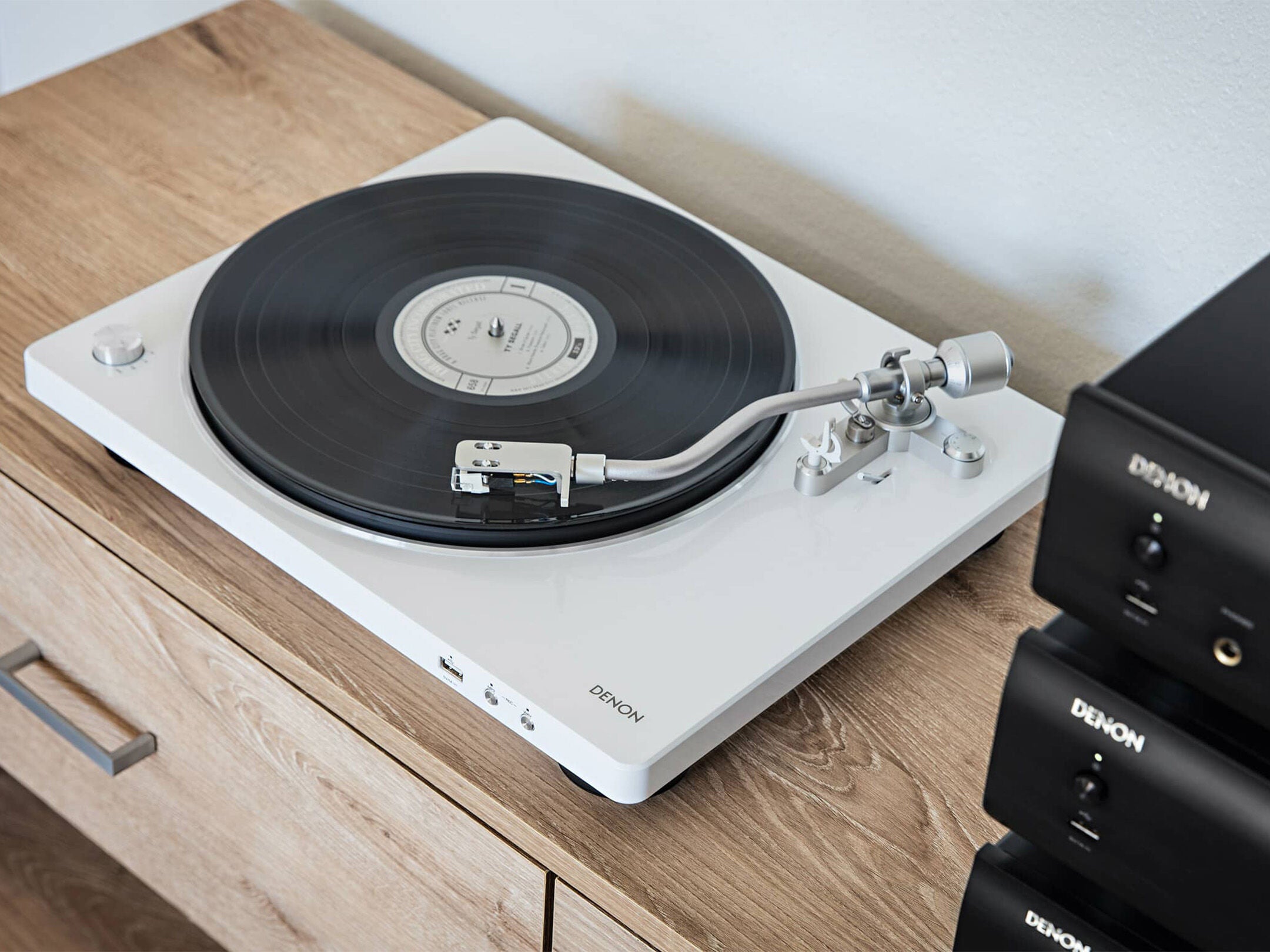 Pick-up Denon DP-450USB alb, vedere de sus, pe masă de lemn, braț și cartuș vizibile, conectivitate USB.