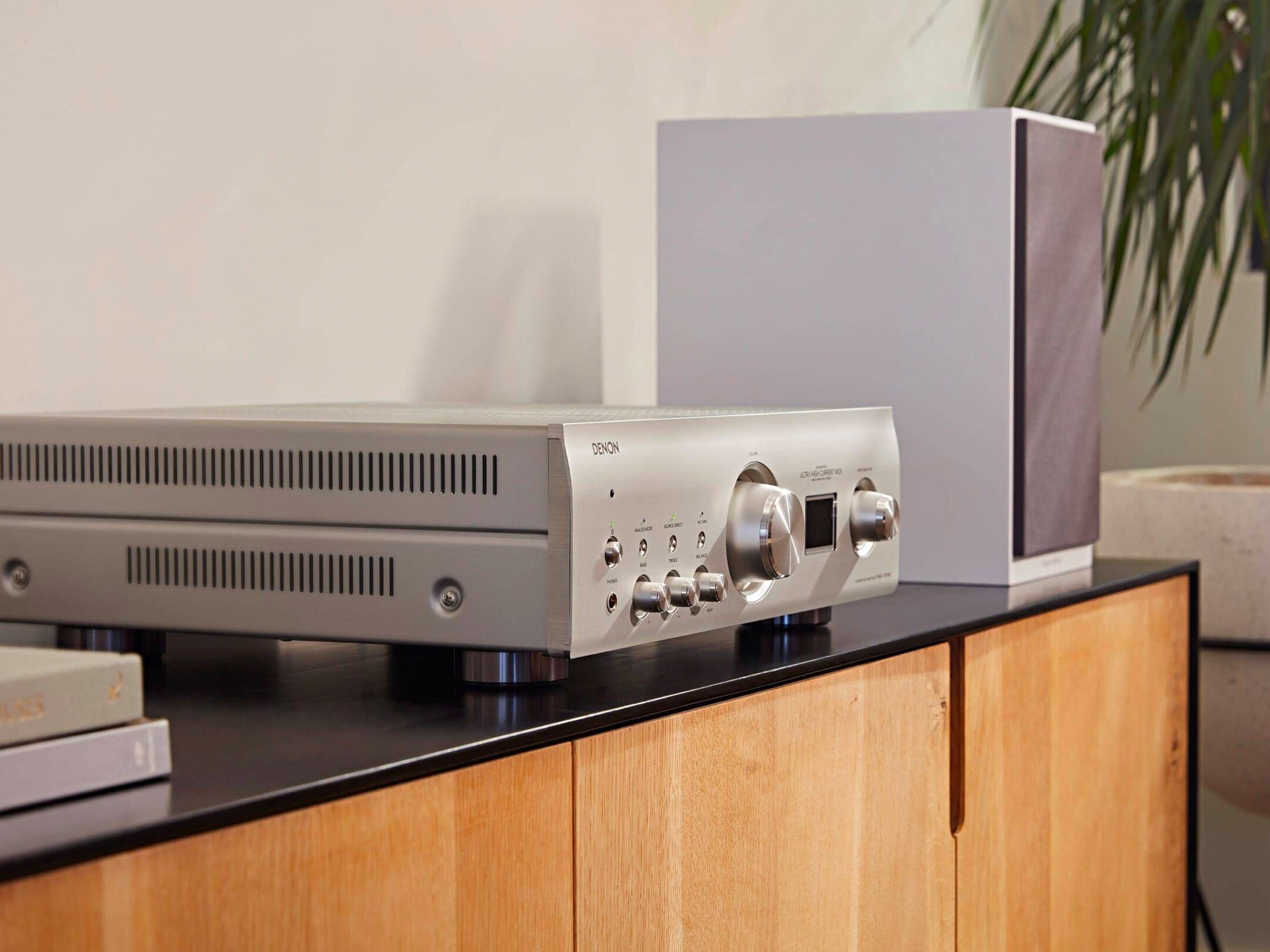 Amplificator Denon PMA-1700NE argintiu, vedere laterală, butoane de control și afișaj vizibile, plasat pe mobilier.