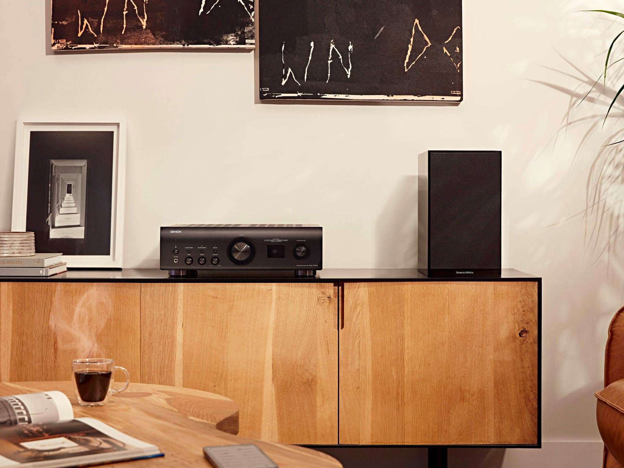 Denon PMA-1700NE Amplificator negru pe mobilier din lemn, lângă o boxă, într-un cadru de cameră modern.