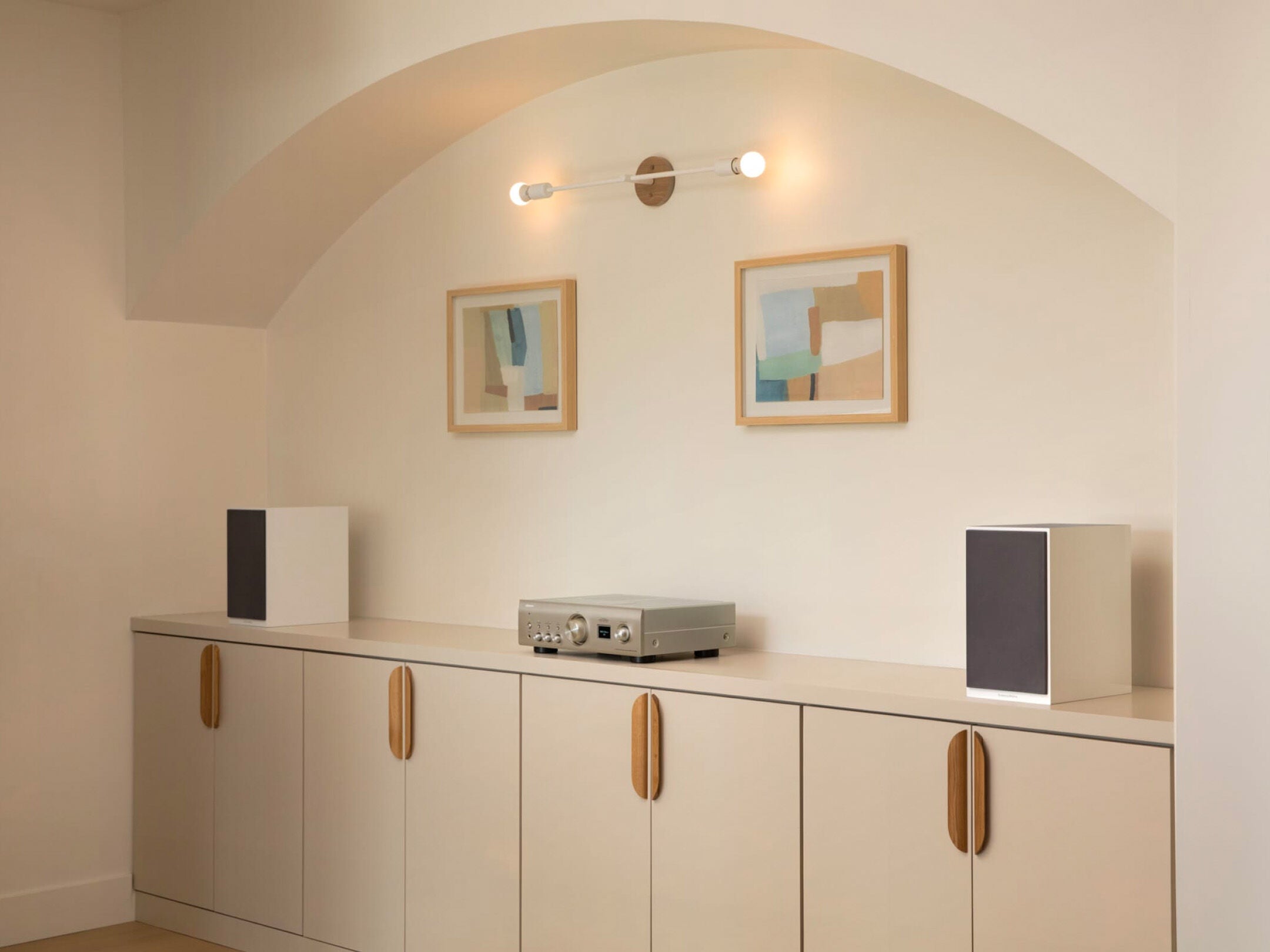 Amplificator Denon PMA-900HNE argintiu, vedere frontală, amplasat pe mobilier, între două boxe albe.