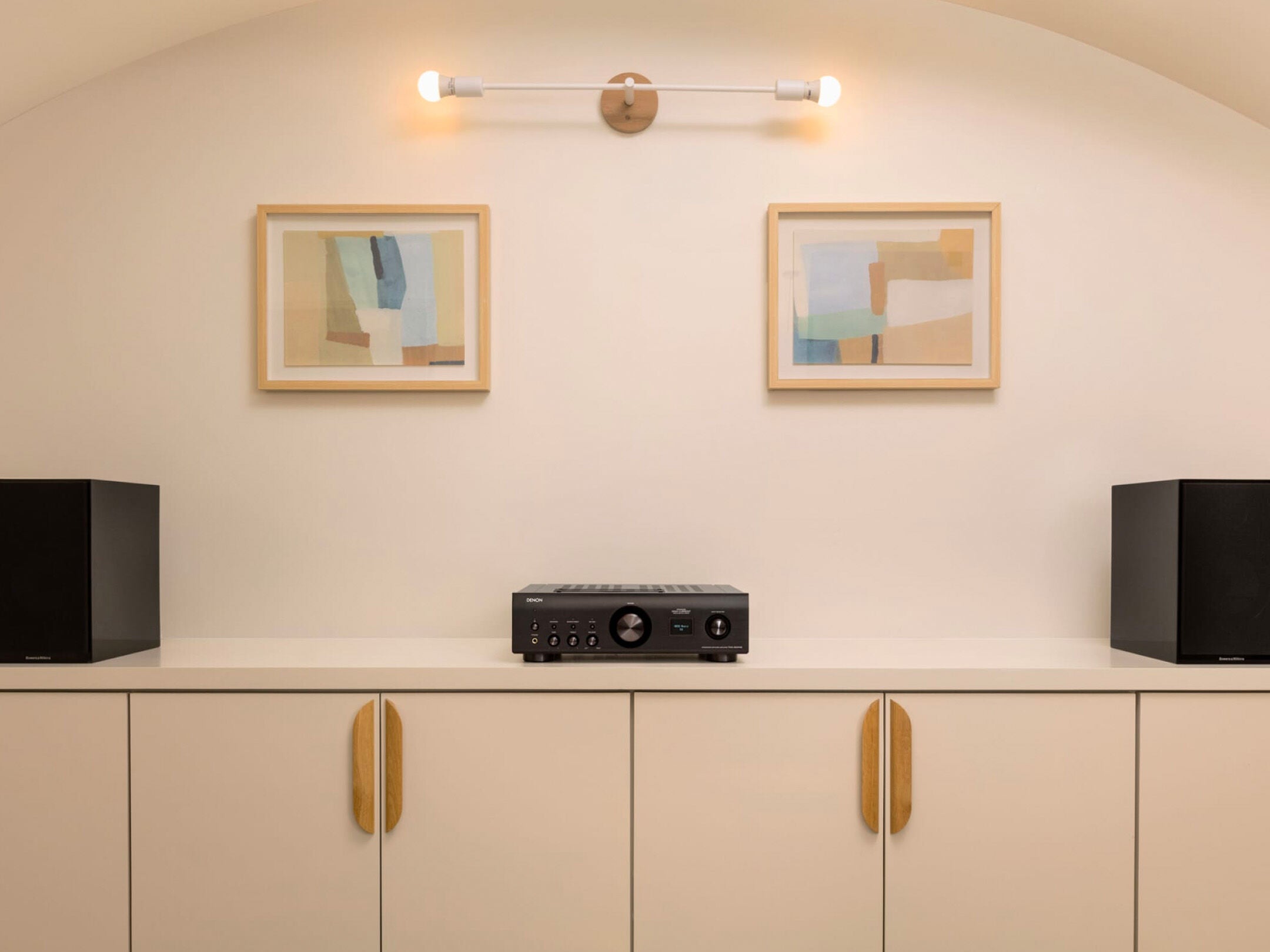 Amplificator Denon PMA-900HNE negru, vedere frontală, așezat pe un dulap alb între două boxe negre.