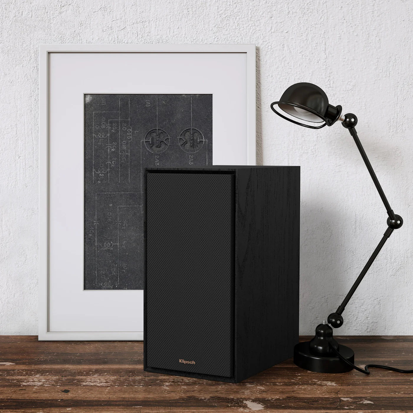 Boxă activă Klipsch R-50PM neagră, vedere frontală cu grilaj montat, amplasată lângă lampă și tablou.