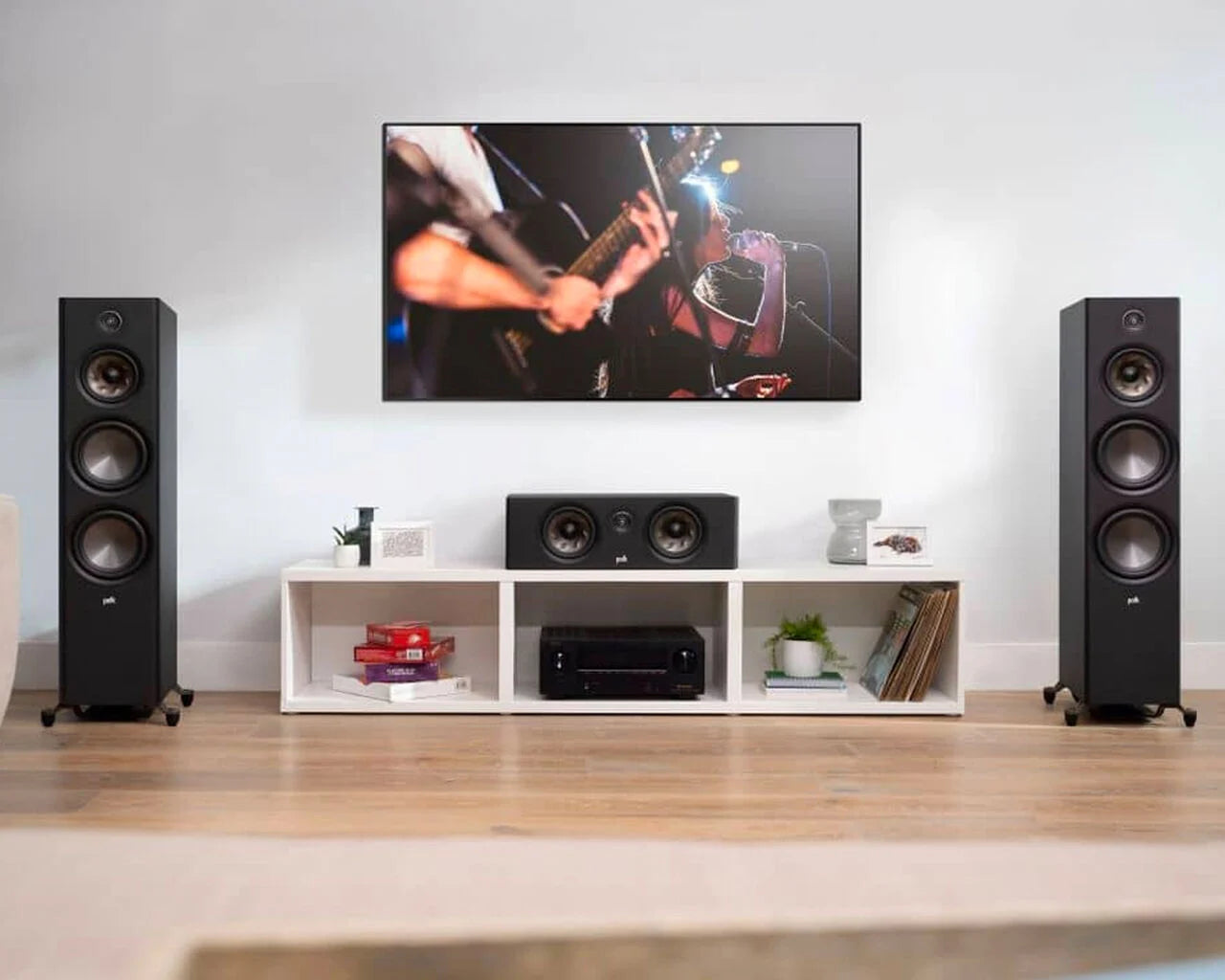 Boxa centru Polk Audio Reserve R300 în living, amplasată pe un raft alb, între două boxe de podea negre.