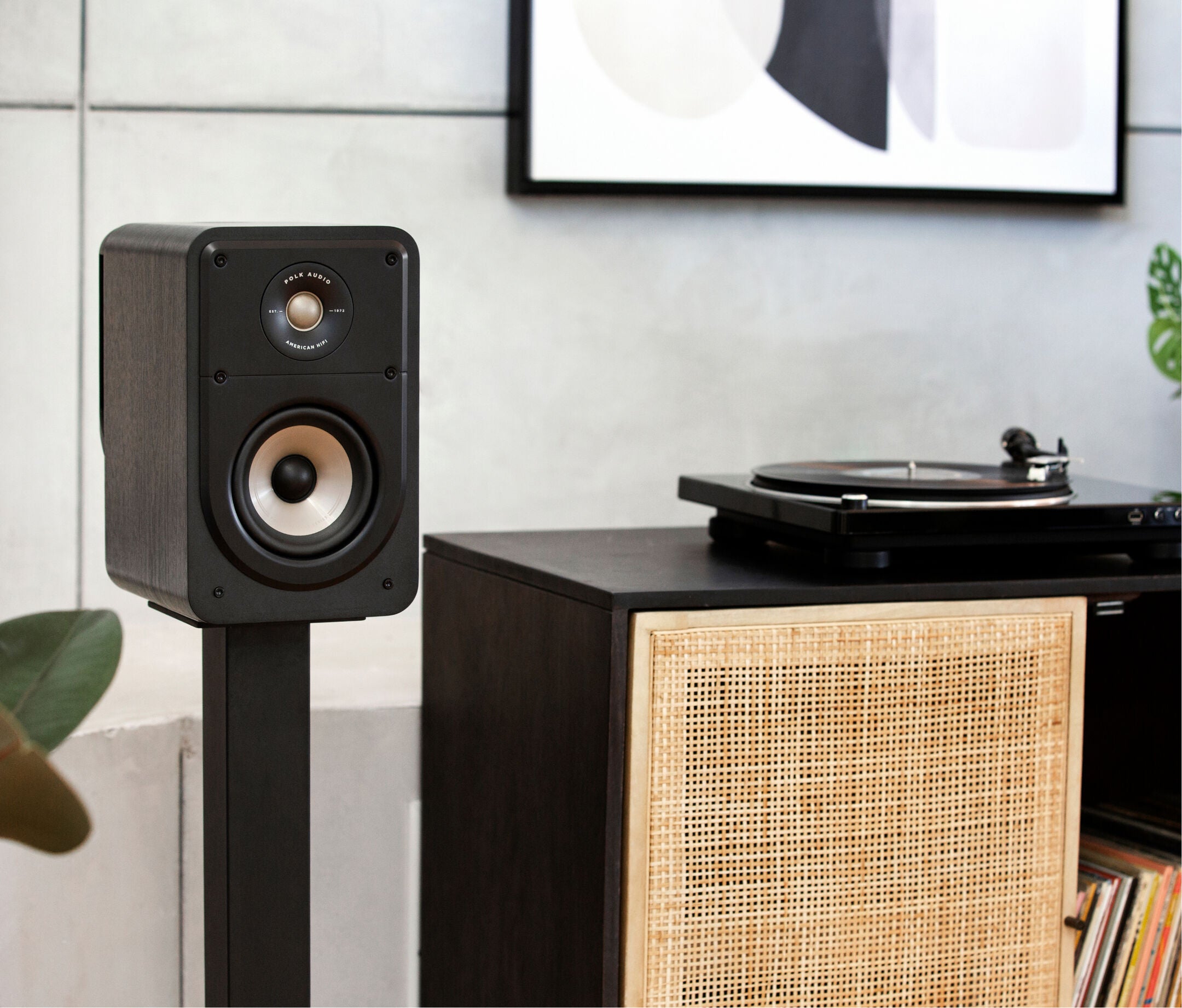 Boxa Polk Audio Signature Elite ES15 neagră, amplasată pe suport lângă un pick-up, într-un mediu interior.