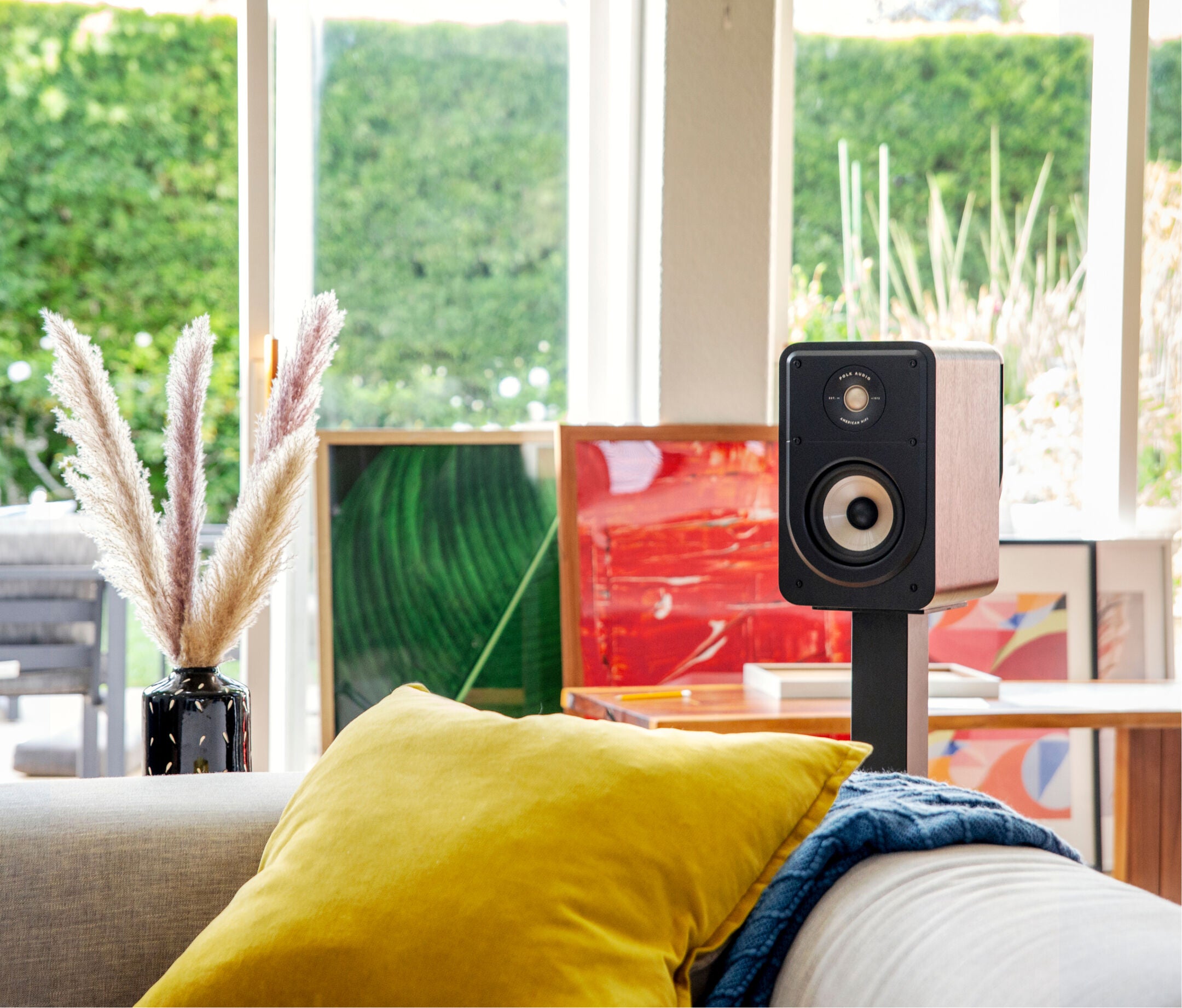 Boxa Polk Audio Signature Elite ES15 neagră, amplasată pe suport într-un living, cu fereastră și decor modern.