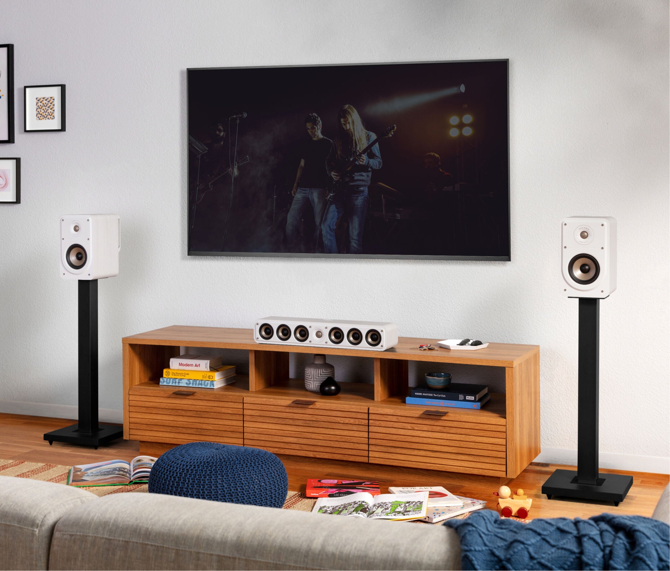 Boxe albe Polk Audio Signature Elite ES15, amplasate pe suporturi negre, într-un living modern, lângă un TV.