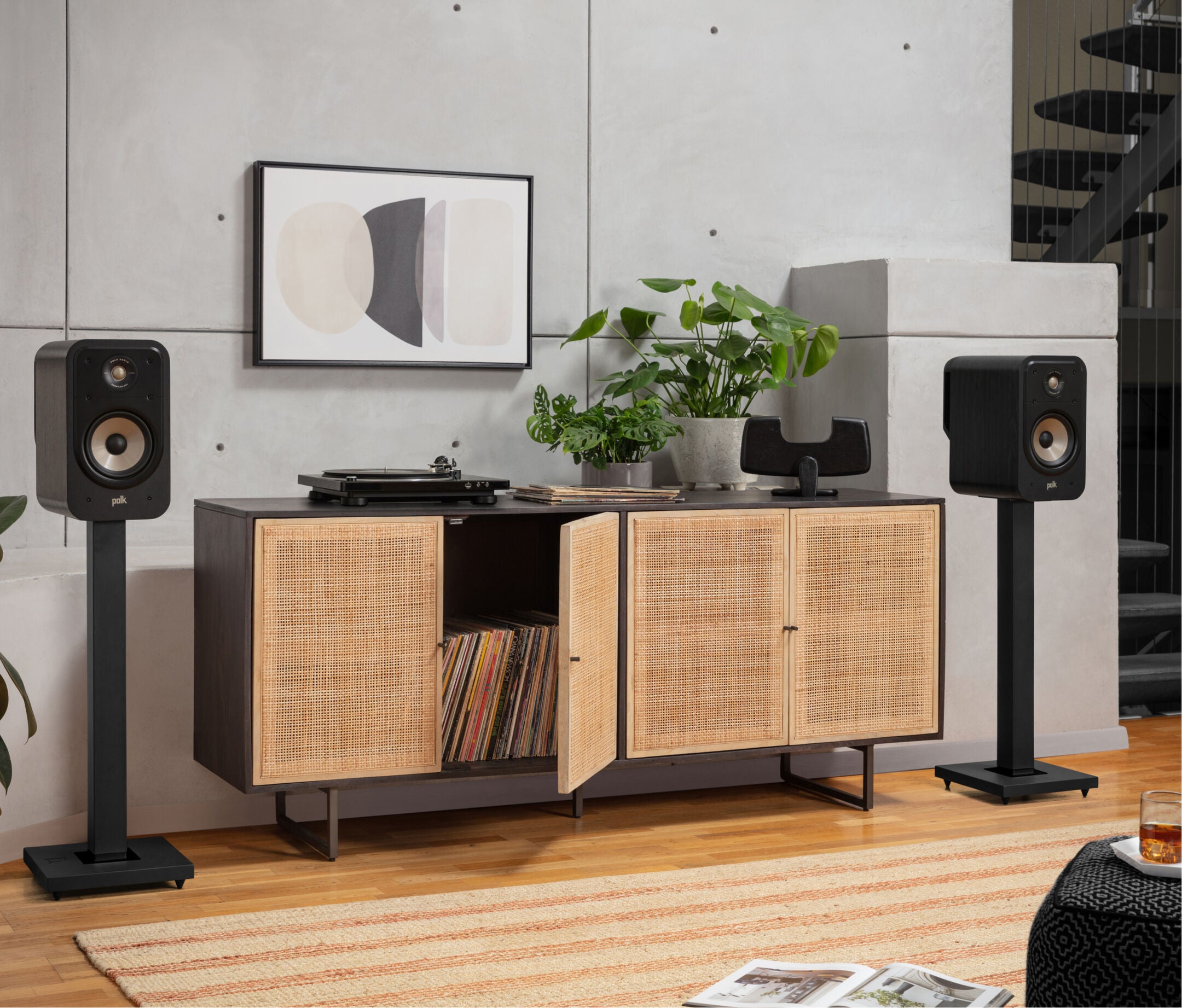Boxe Polk Audio Signature Elite ES20 negre, amplasate pe suporturi lângă un mobilier din lemn, într-un living modern.