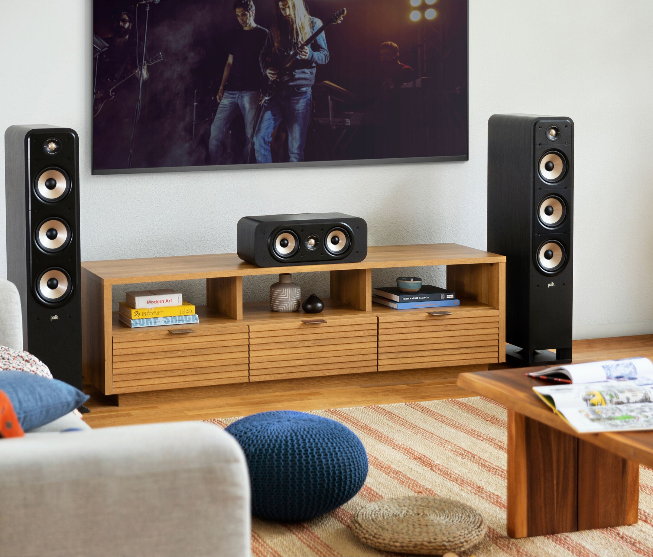 Boxa centru Polk Audio Signature Elite ES30 neagră, amplasată pe un raft de lemn, între două boxe de podea.