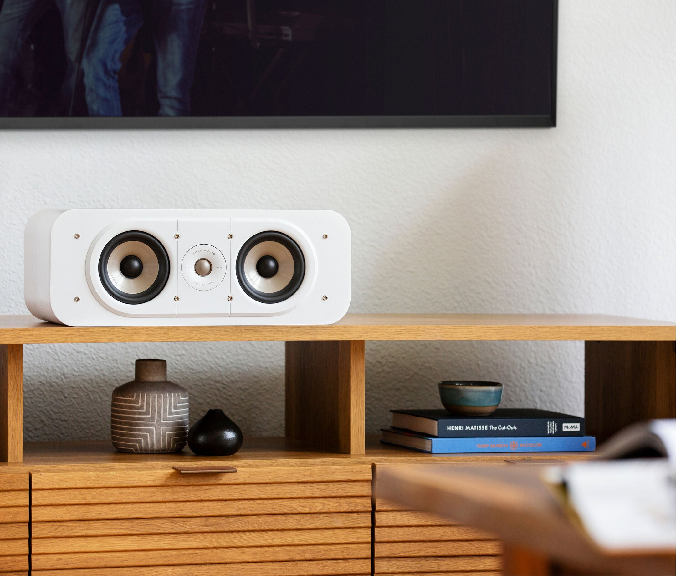 Boxa centru Polk Audio Signature Elite ES30 albă, amplasată pe un raft de lemn, cu două difuzoare vizibile.