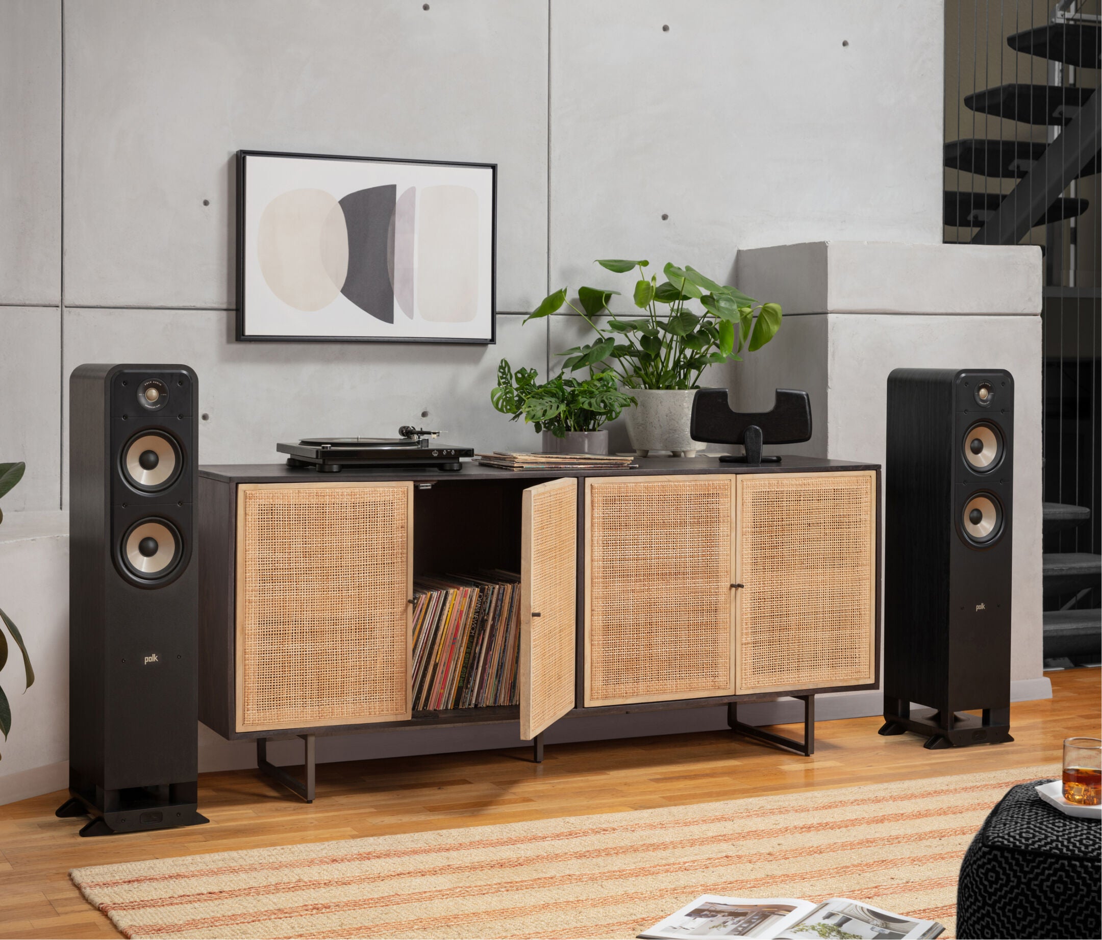 Boxe de podea Polk Audio Signature Elite ES55 negre, amplasate lângă un mobilier cu plante și un pick-up.
