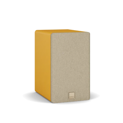 Boxă de raft Dali Kupid Golden Yellow, vedere frontală-stânga, grilaj textil bej și logo DALI vizibil.