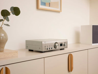 Denon PMA-900HNE Amplificator argintiu, vedere laterală, afișaj digital și butoane de control vizibile.