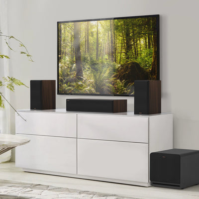 Subwoofer Klipsch RP-1200SW negru, vedere frontală în setup home theater, lângă dulap TV alb.