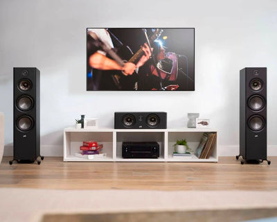 Boxa centru Polk Audio Reserve R300 în living, amplasată pe un raft alb, între două boxe de podea negre.