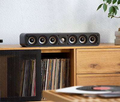 Boxa centru Polk Audio Signature Elite ES35, negru, amplasată pe un raft de lemn, cu șase difuzoare vizibile.