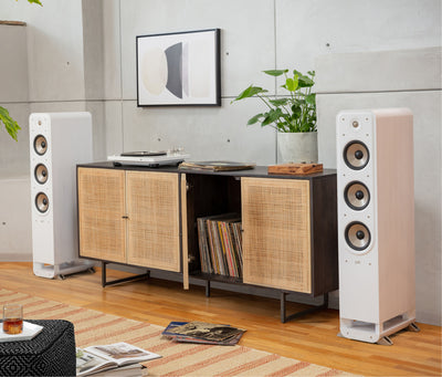 Boxe de podea Polk Audio Signature Elite ES60 albe, plasate într-un living modern, lângă un dulap cu discuri.